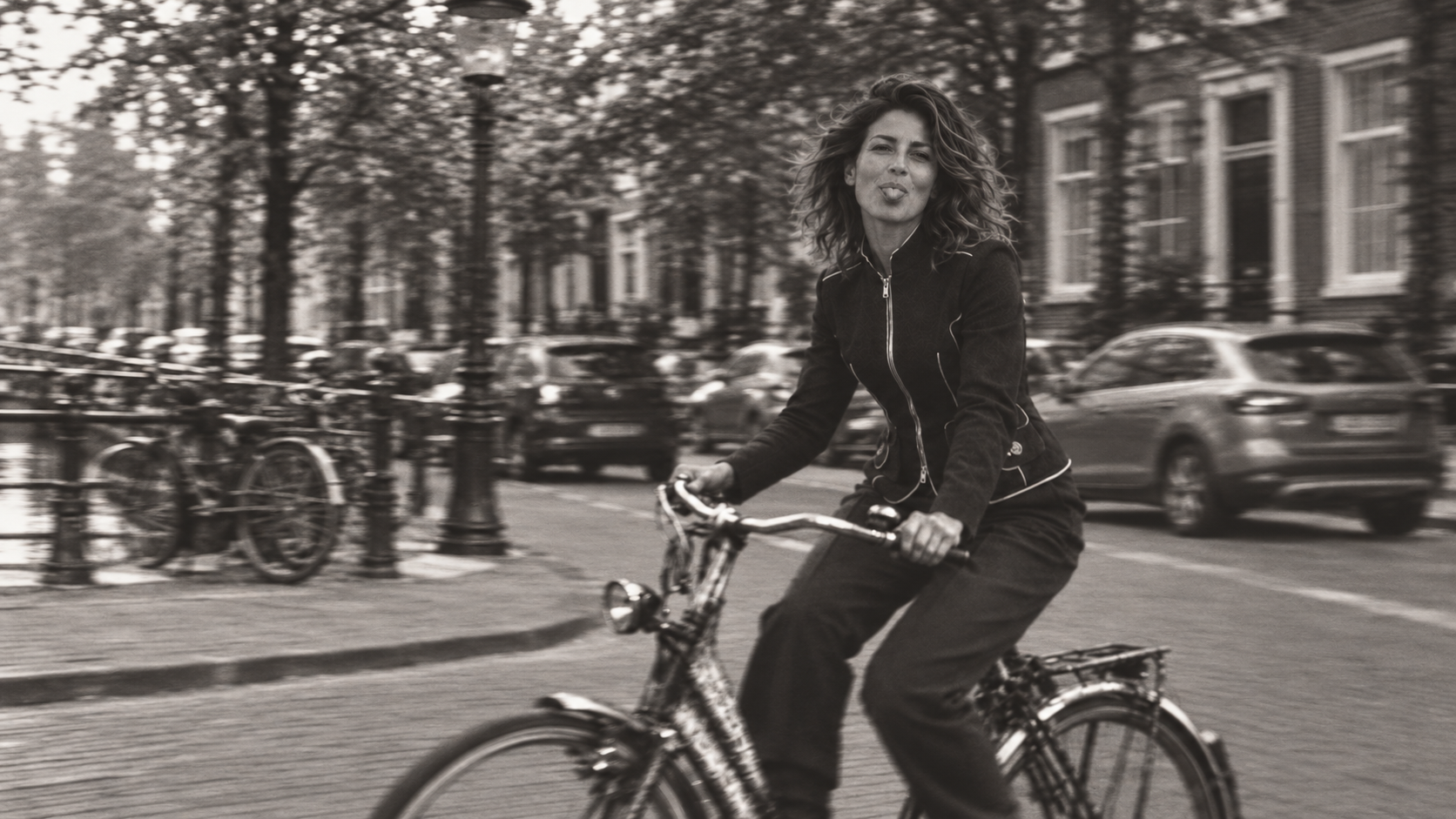 Model in a black jacket cycling through an Amsterdam street